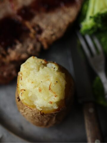 a baked potato on a pewter plate with antique knife and fork
