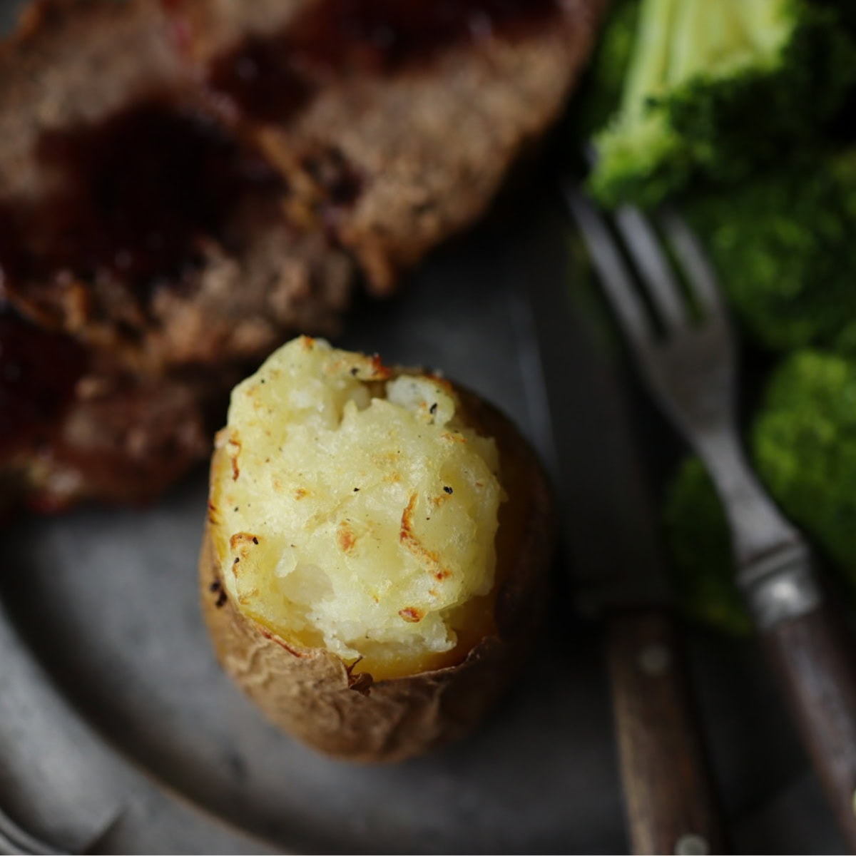 a baked potato on a pewter plate with antique knife and fork