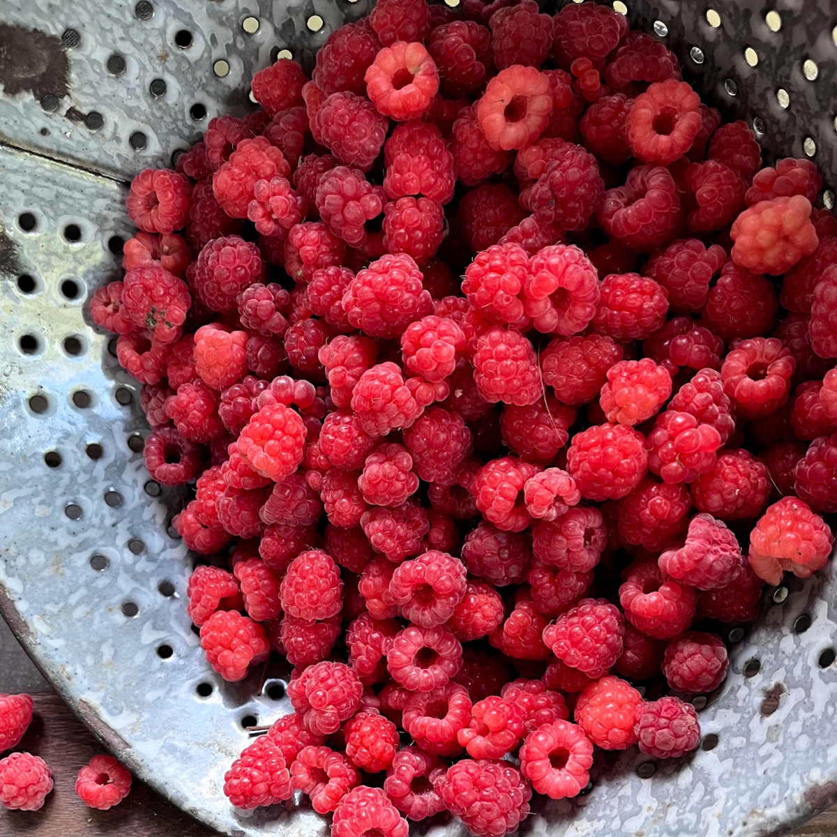 an old fashioned colander full of raspberries